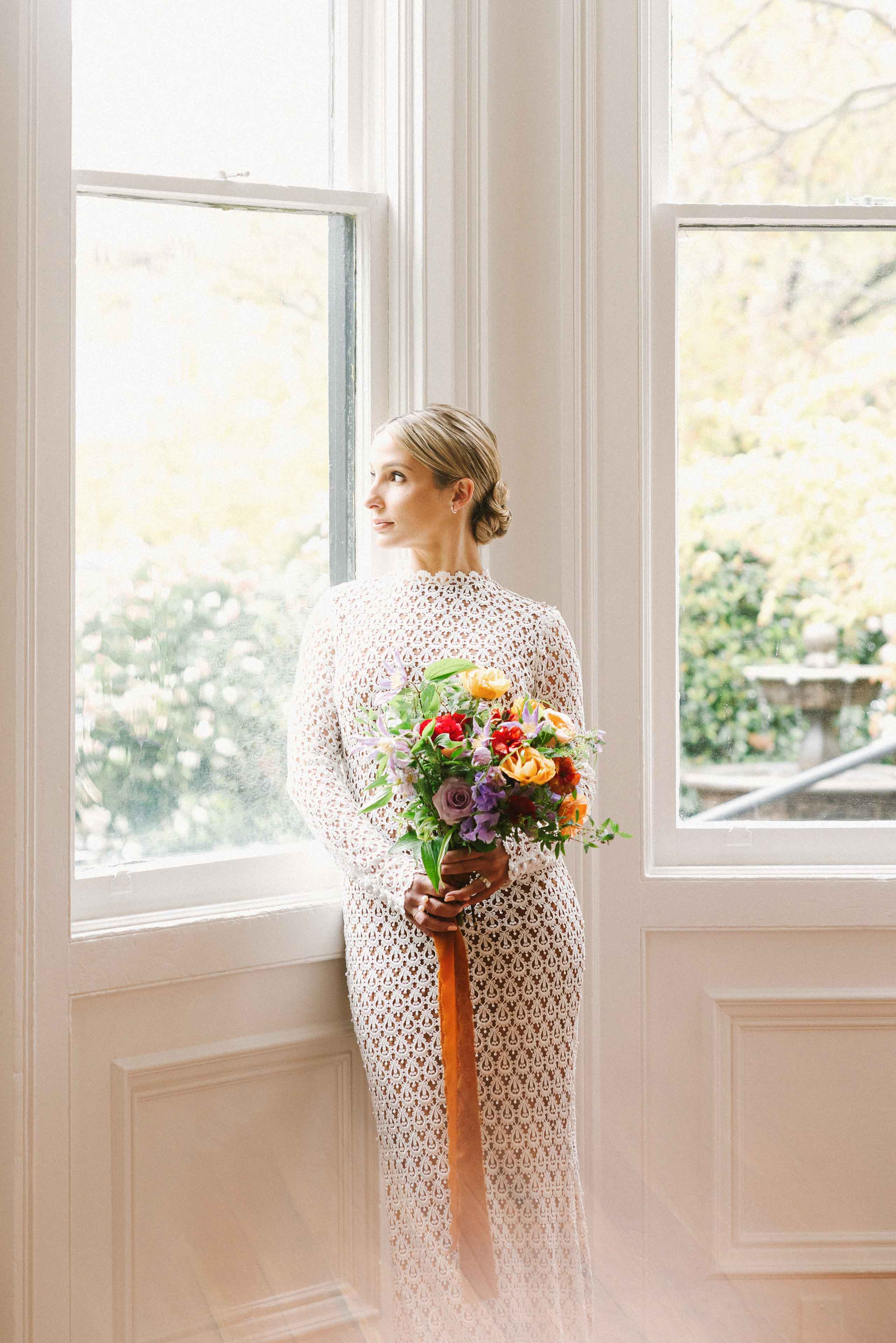 Bride posing with bouquet next to window